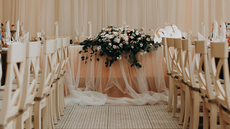 A beautifully decorated aisle of a wedding banquet hall leads to a stage adorned with a floral centrepiece 