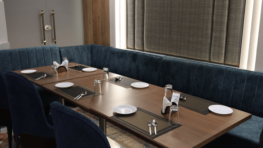 A cosy dining booth features a wooden table alongside a curved blue velvet bench - Lords Inn Sangam, Bhopal