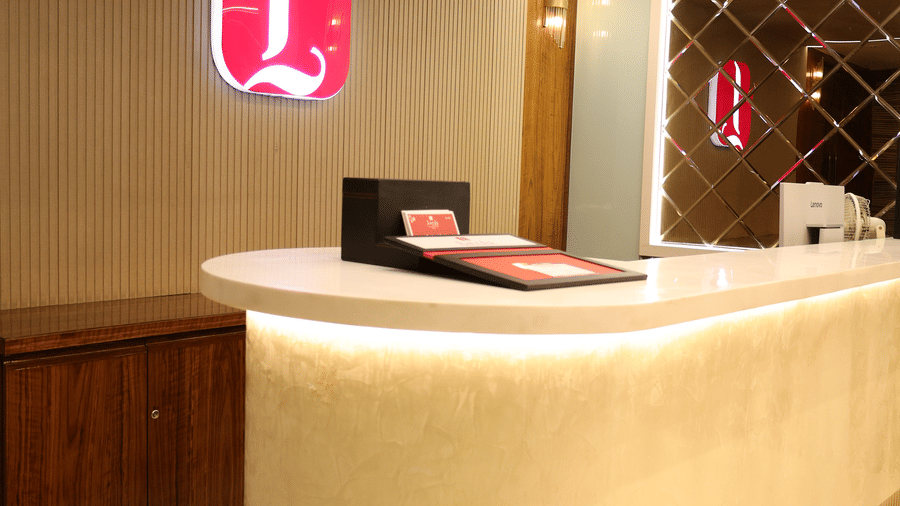 A sleek, modern white reception desk sits under warm lighting with a red logo - Lords Inn Sangam, Bhopal