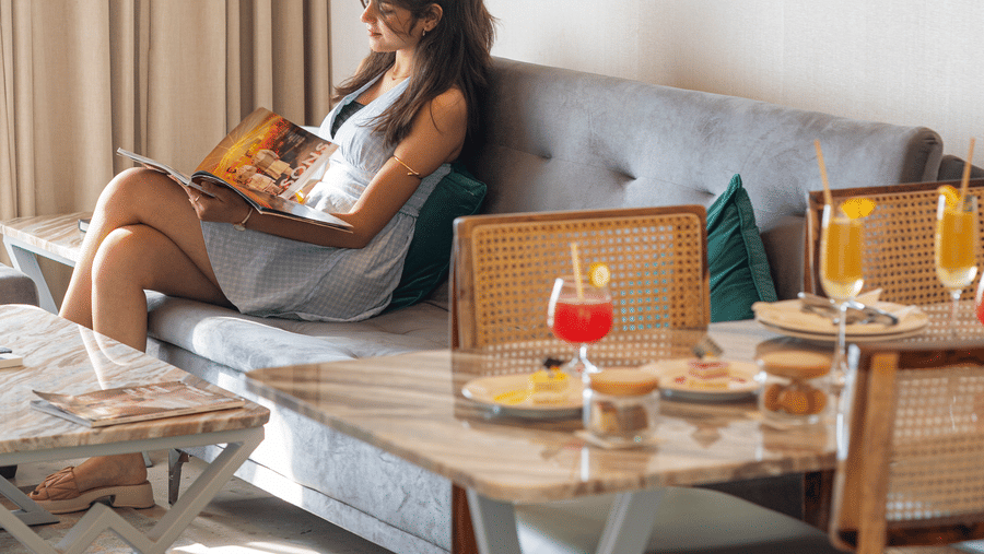 A woman sitting on a sofa in Sajjan Villa at Bamboo Saa Resort and Spa, Udaipur. The room also features a dining space with table and chairs.