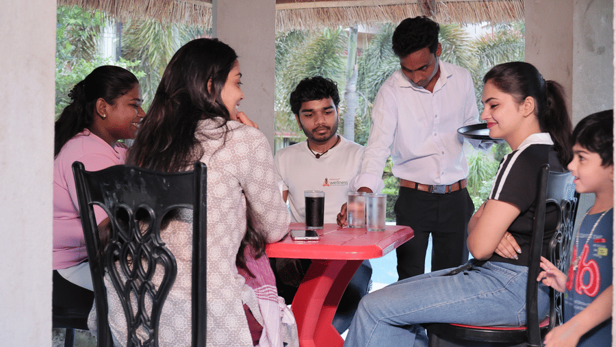 A group of 5 people, gathered around a table under a thatched roof structure at Shophori Wellness Retreat, Bolpur.