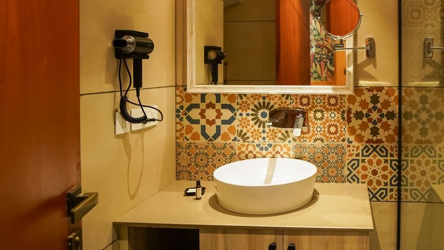 A modern bathroom features a vanity with a round basin sink, a large mirror, and a wall-mounted faucet, set against light-coloured walls | Deluxe Room with Valley View | Sukama Resort & Spa, Nainital