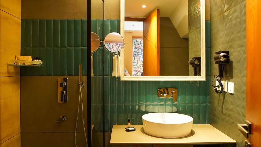 A bathroom with a modern sink vanity, a large mirror, and a toilet visible in the reflection | Deluxe Room | Sukama Resort & Spa, Nainital