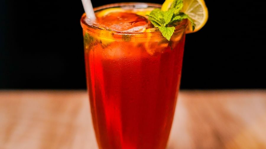 A tall glass containing a vibrant red beverage, garnished with a lime slice and a straw, set on a wooden surface | Sukama Resort & Spa, Nainital