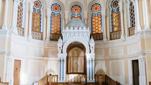 Interior of Paradesi Synagogue in Kochi with wooden benches, ornate ark with Star of David curtain, and stained glass windows above.
