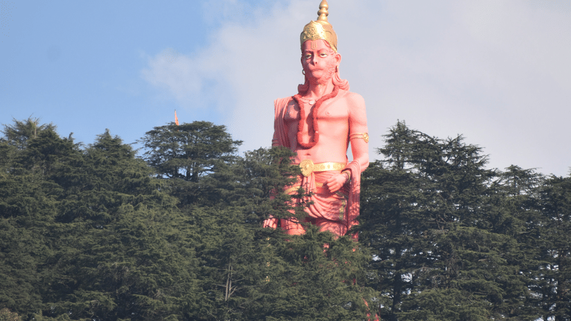 A view from a afar of the 108-feet Hanuman statue surrounded by trees in Jakhu Hills. This is one of the best places to see in Shimla to be astounded by the beauty nature and human inginuity.