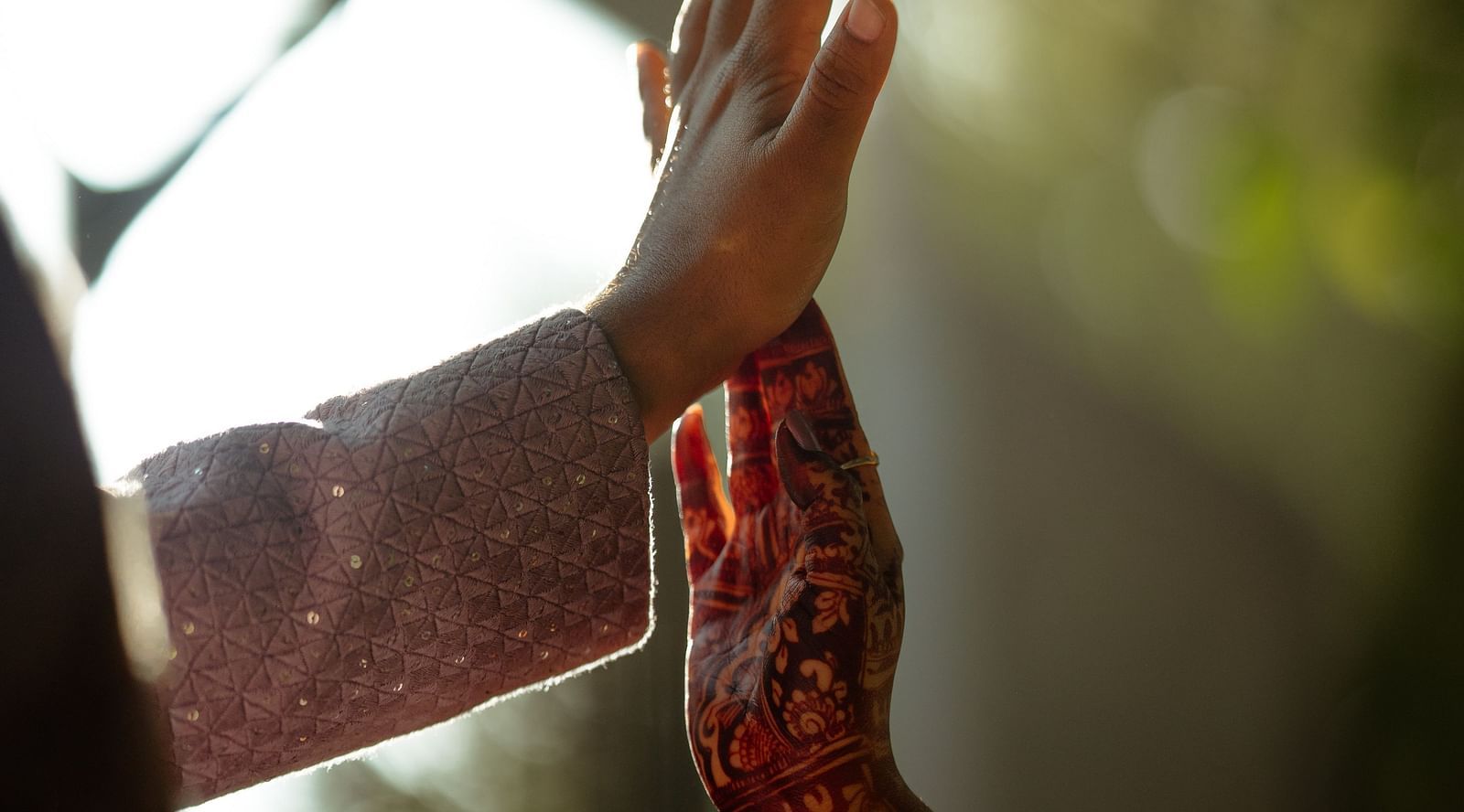 image of the hands of a couple with a beautiful blurry backdrop of sunlight cannopy in the back