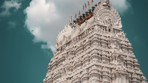 A view from below of the intricate art on the gopuram of the temple in Tirupati, with a cloud behind it.