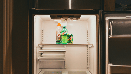A view of a an open, stainless steel refrigerator with multiple empty shelves and one bottle of liquid visible in the door compartment.