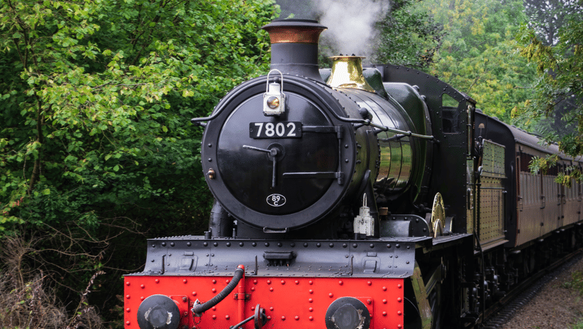 An old train running on charcoal going through a forest