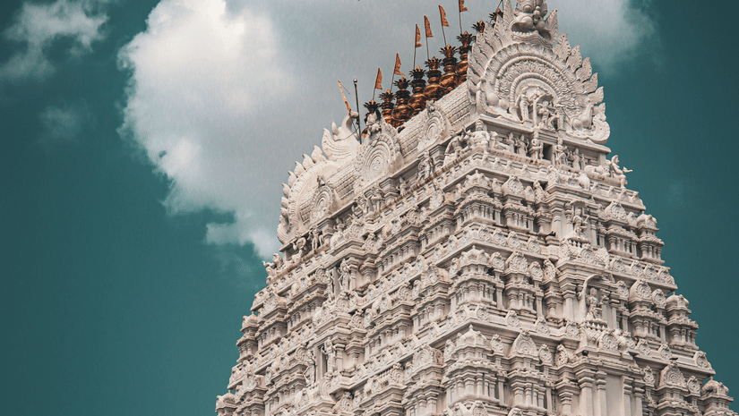 A view from below of the intricate art on the gopuram of the temple in Tirupati, with a cloud behind it.