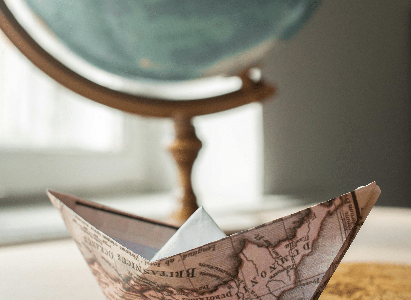 A paper boat made from a map, with a globe in the background