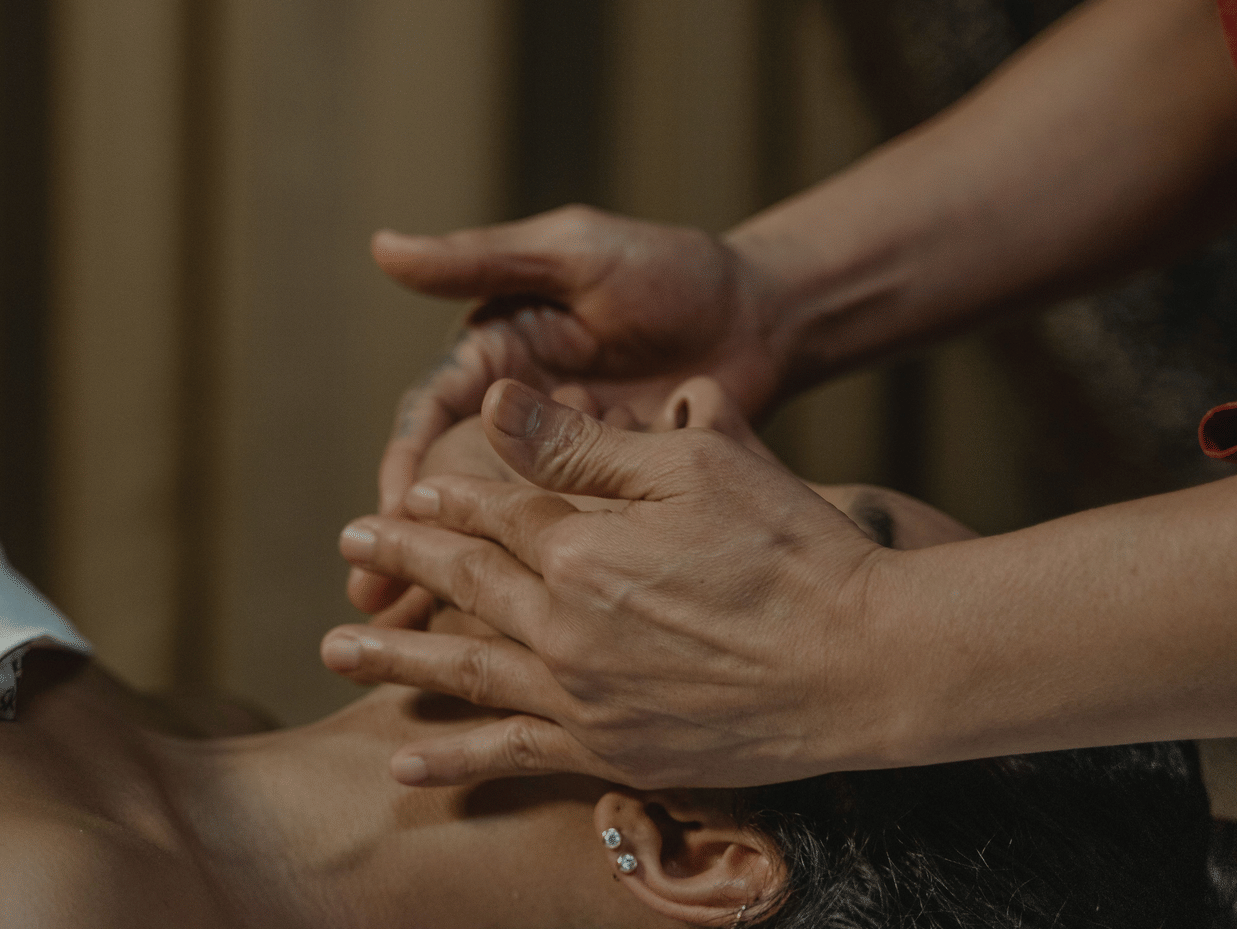 A person lying down on a spa bed receiving a gentle face massage by a masseuse.