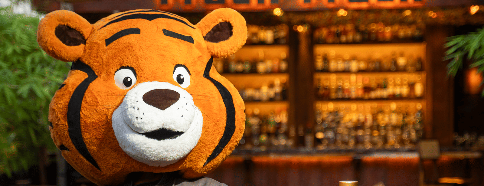 A person in a tiger mascot costume standing near a dining table at Infiniti Hotel, Indore.