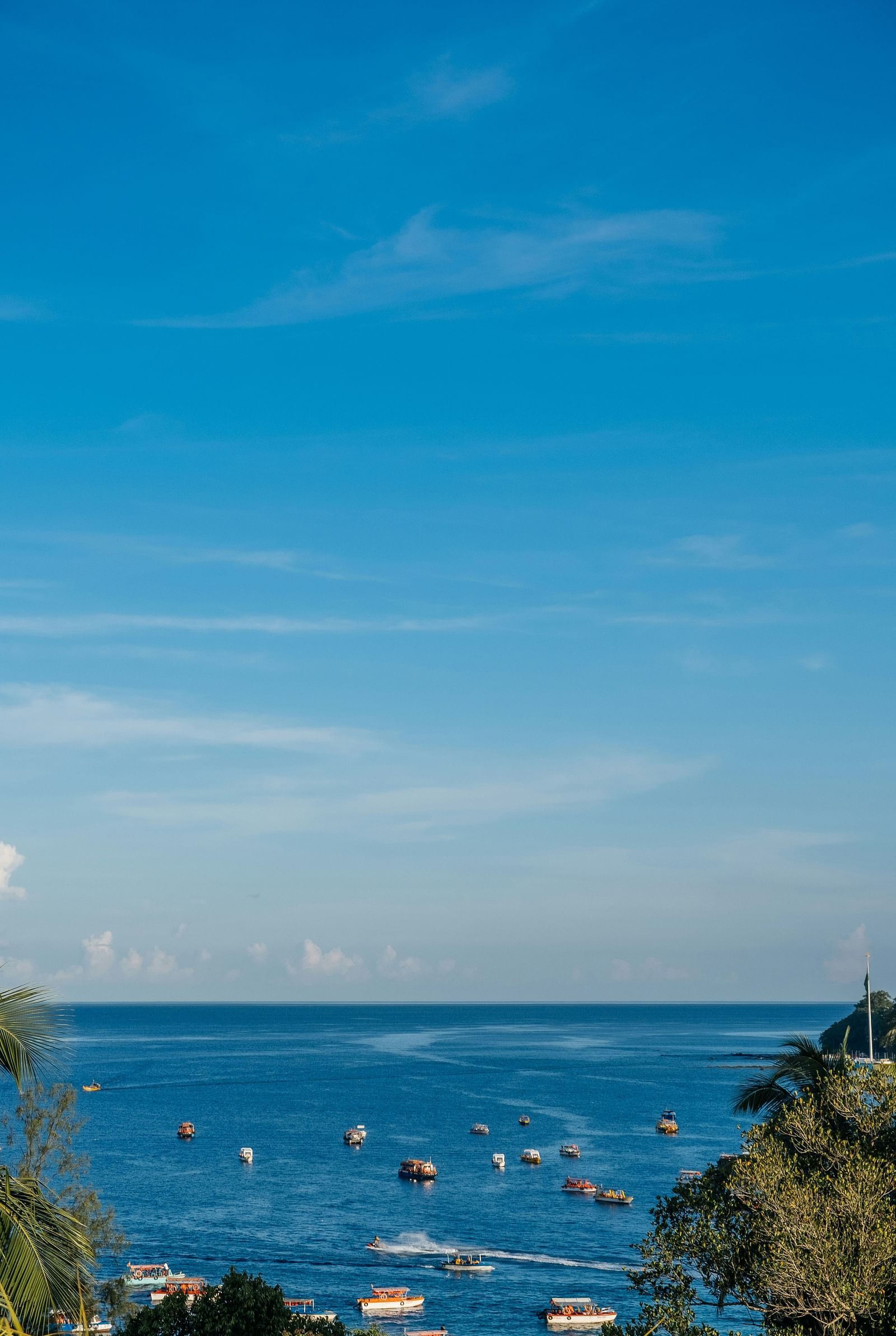A serene view of a coastal skyline with several boats scattered on the blue water under a clear sky