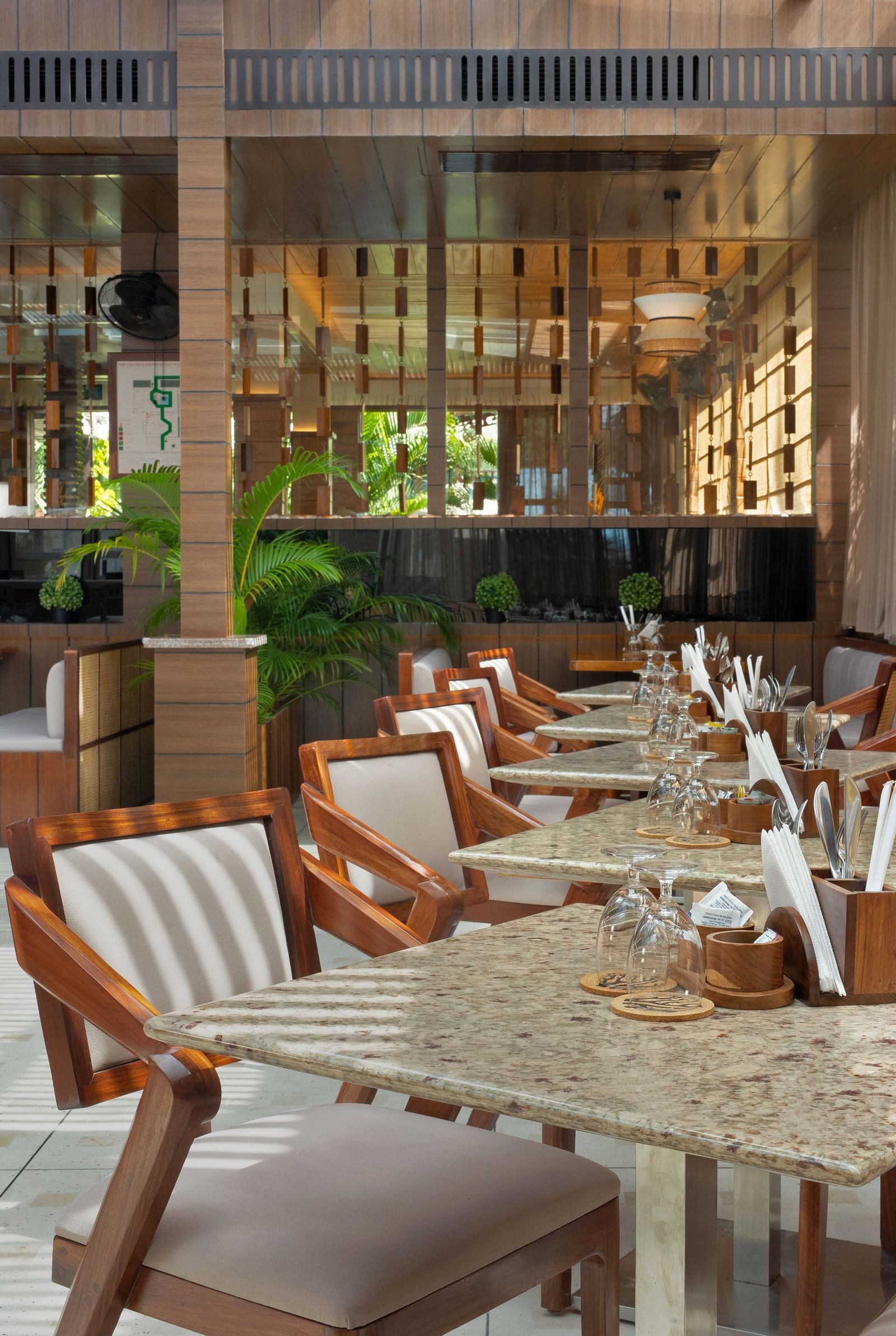5th Bistro Cafe and Bar at Coral Reef Resort & Spa in Havelock featuring a dining area with outdoor seating, featuring wooden tables and striped chairs. The space is set in a lush garden with ample greenery, creating a comfortable, scenic setting - Coral R