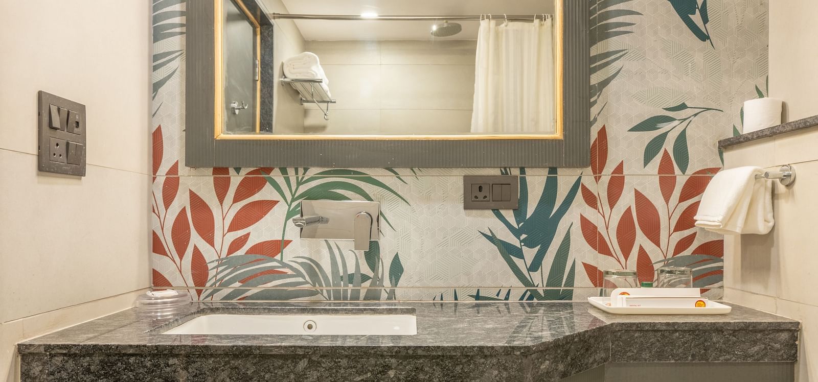 A toilet and washbasin with mirror in a tiled flowery bathroom at Hotel Highway King, Jaipur.