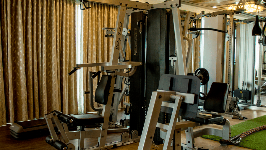 The fitness centre at the Benzz Park, Vellore, featuring a fitness equipment in dimly lit interiors.