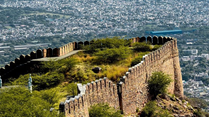 A scenic view of an ancient fort on a hilltop, overlooking a city with distant mountains in the background.