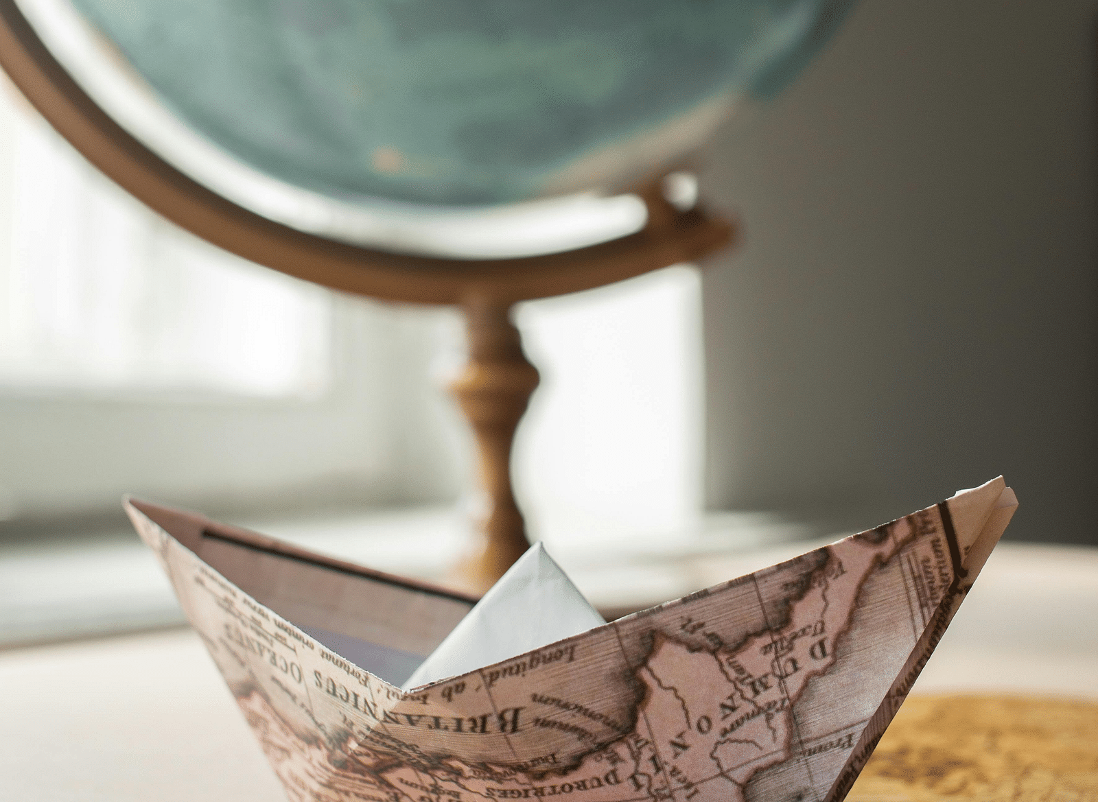 A paper boat made from a map, with a globe in the background