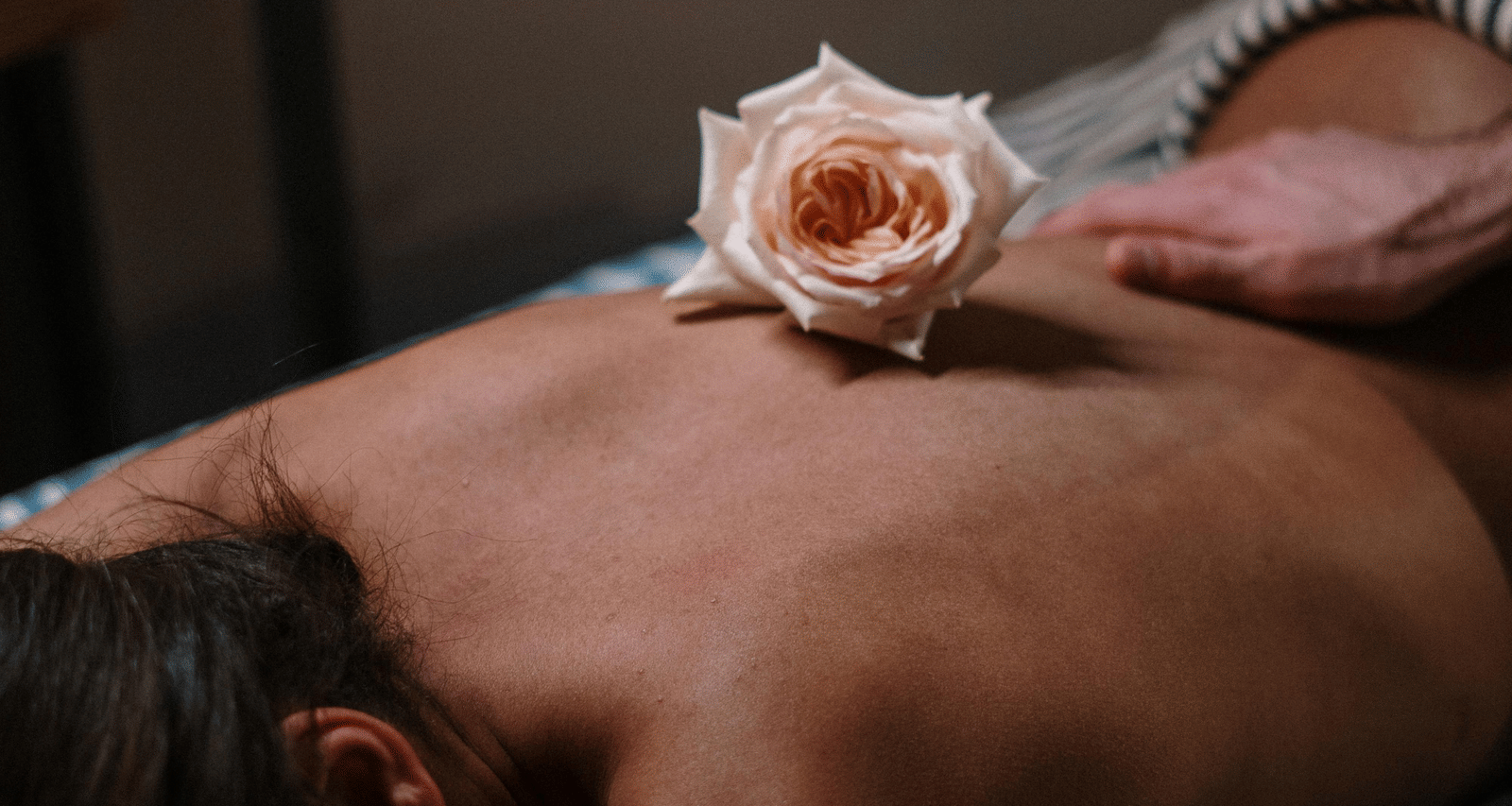 A person receiving a back massage, adorned with a pink rose on their back.