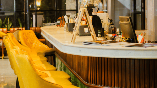A stylish bar counter at Hotel Polo Towers with yellow bar stools and a green tiled base.