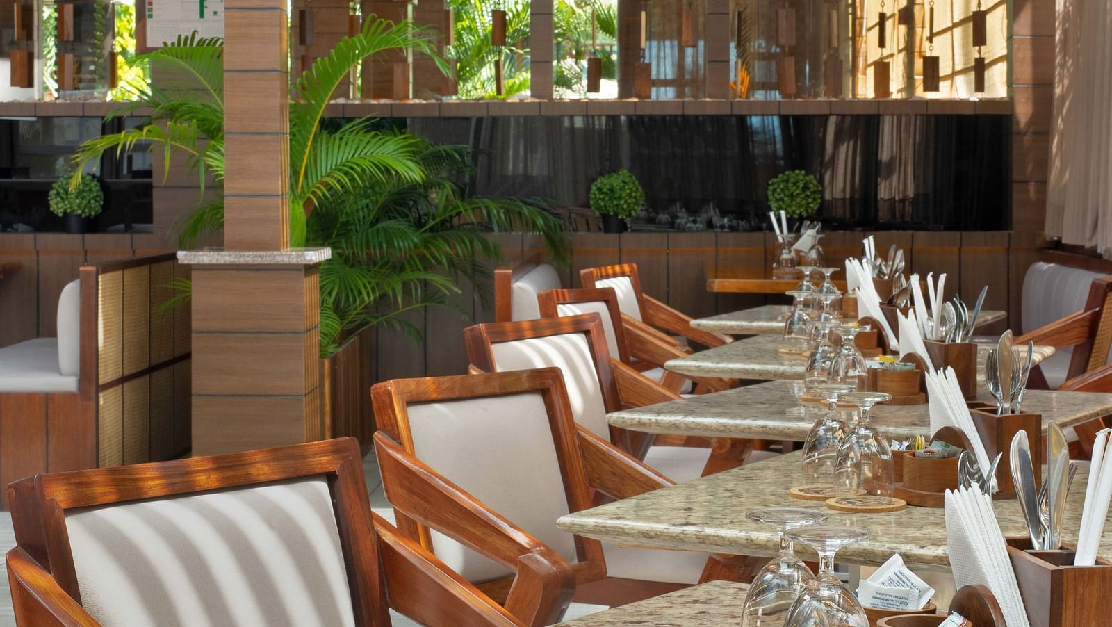 5th Bistro Cafe and Bar at Coral Reef Resort & Spa in Havelock featuring a dining area with outdoor seating, featuring wooden tables and striped chairs. The space is set in a lush garden with ample greenery, creating a comfortable, scenic setting - Coral R