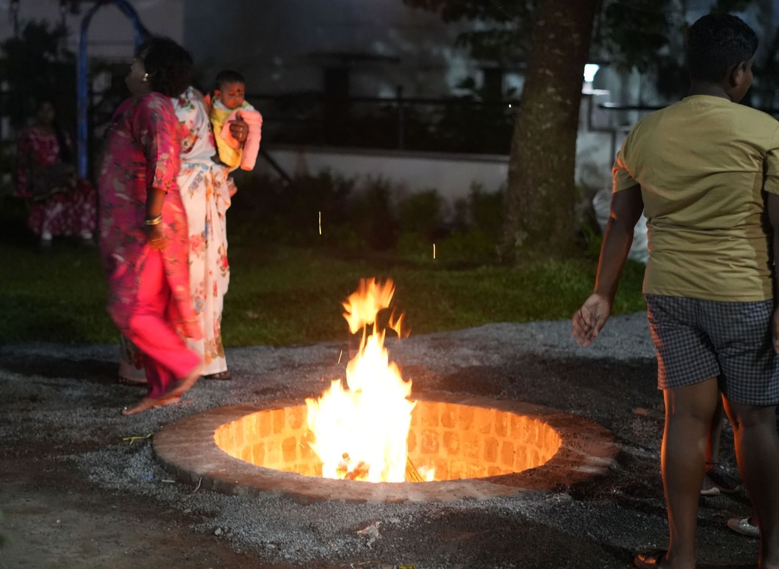 A portrait shot of the bonfire at the WOW Naturefull Resorts with a group of people surrounding it during the late evening.