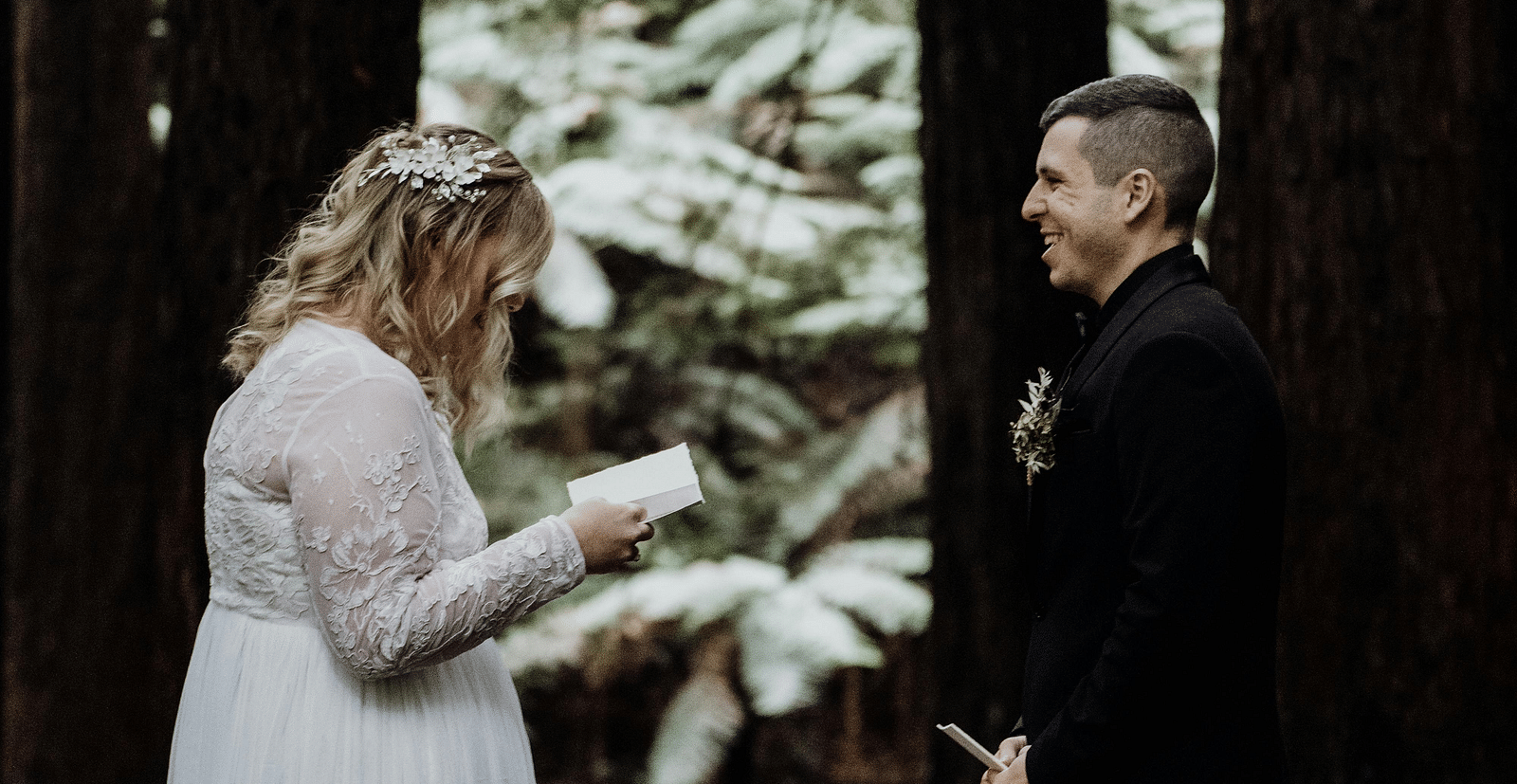 A bride and a groom standing in a forest with tall trees in the backdrop - The Groveland Hotel.