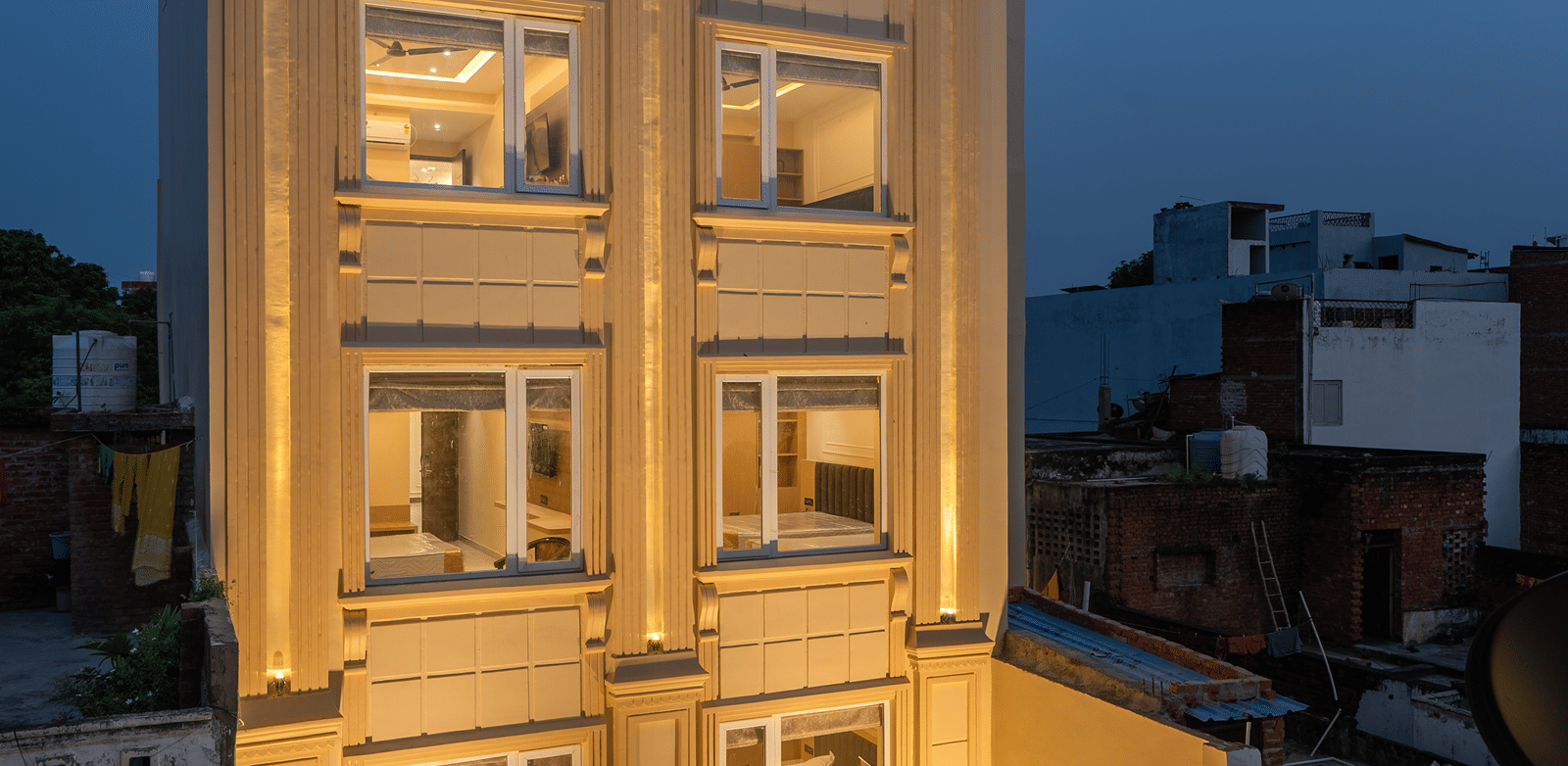 Perfectstayz Premium Lavender, Varanasi at twilight, a cream 5-storey building with Corinthian pilasters, glowing room windows, and a marble-floored glass entrance.