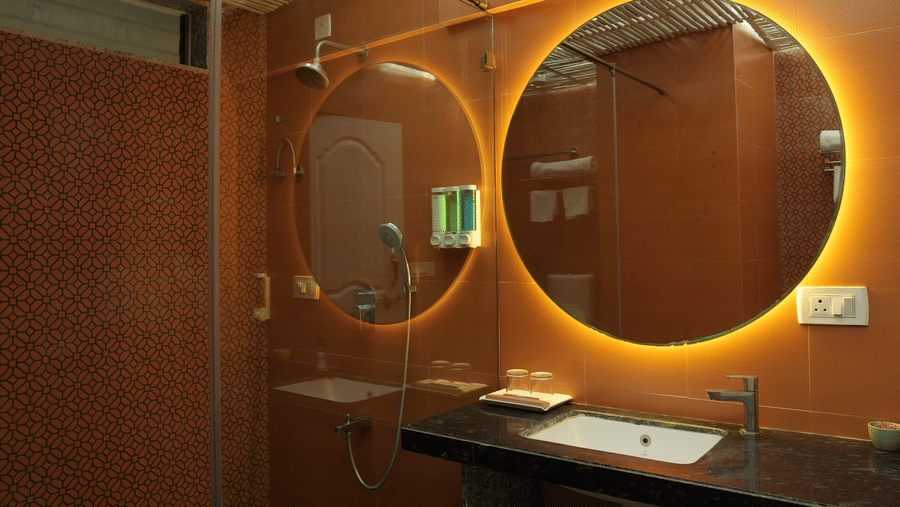A bathroom at Oceanature Resort, Alibaug featuring a circular mirror with backlighting, a sink counter, and a bamboo-style ceiling.
