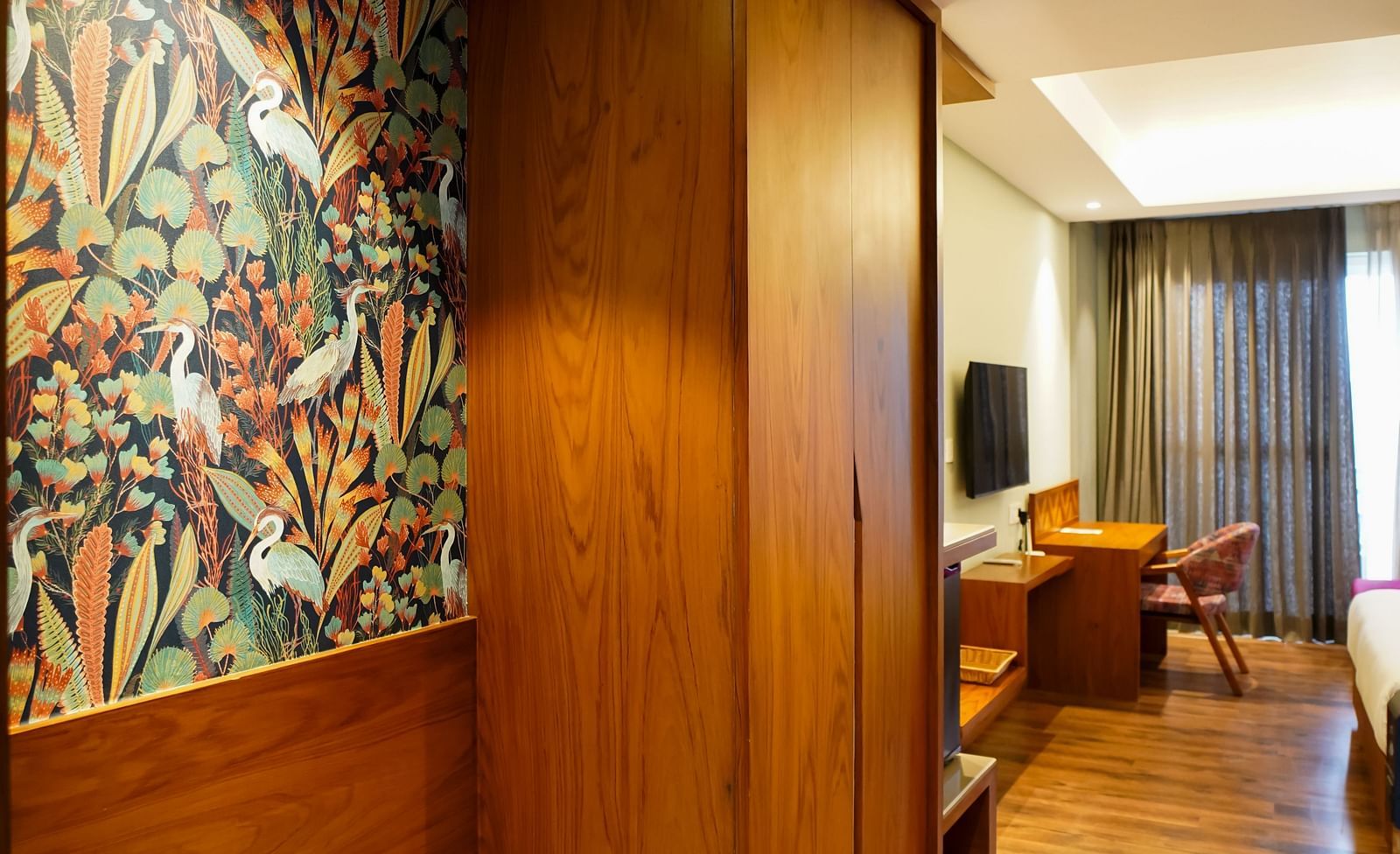 A well-lit hotel room entrance area features wooden panelling, a small bench, and a glimpse into the main room | Deluxe Room with Himalayan View | Sukama Resort & Spa, Nainital