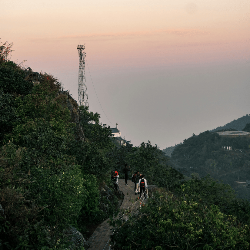 Visitors walking along a scenic trekking trail at Parasnath Hill surrounded by dense greenery and hillside views.