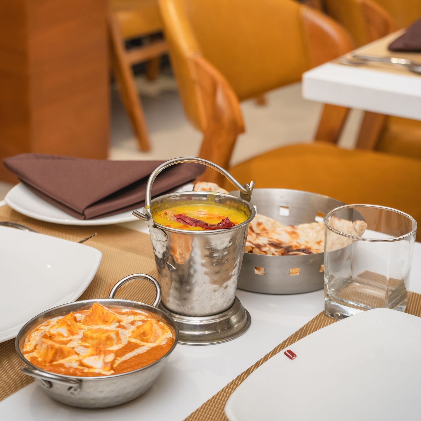 Bowls of food and drinks are arranged on a set table in a restaurant with empty chairs - Lords Eco Inn Ambaji.