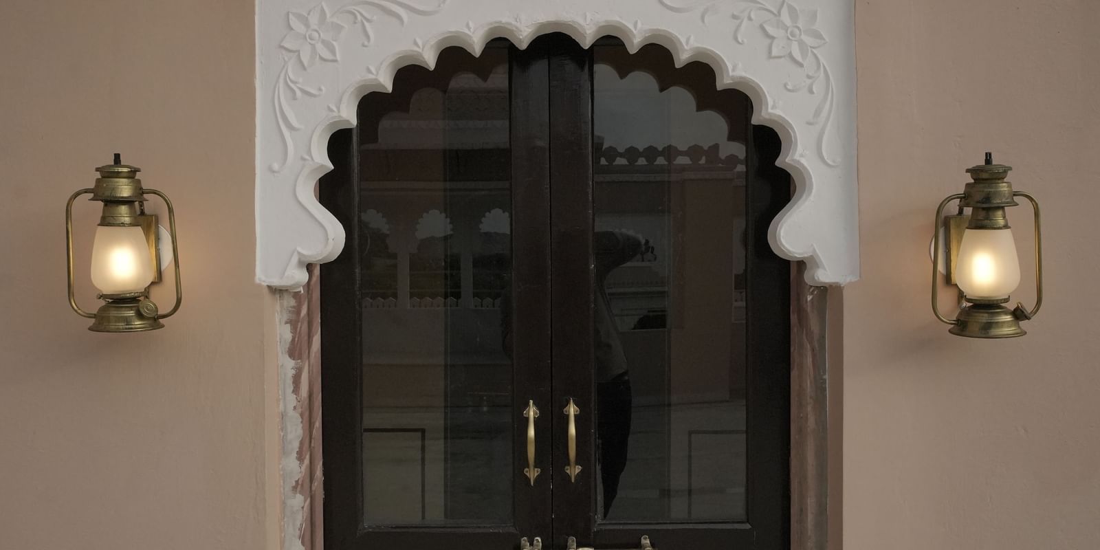 A grand bedroom in the Terrace Suite at Mahendra Niwas, featuring a large bed with a decorative headboard and white bedding. A chandelier hangs from the ceiling.