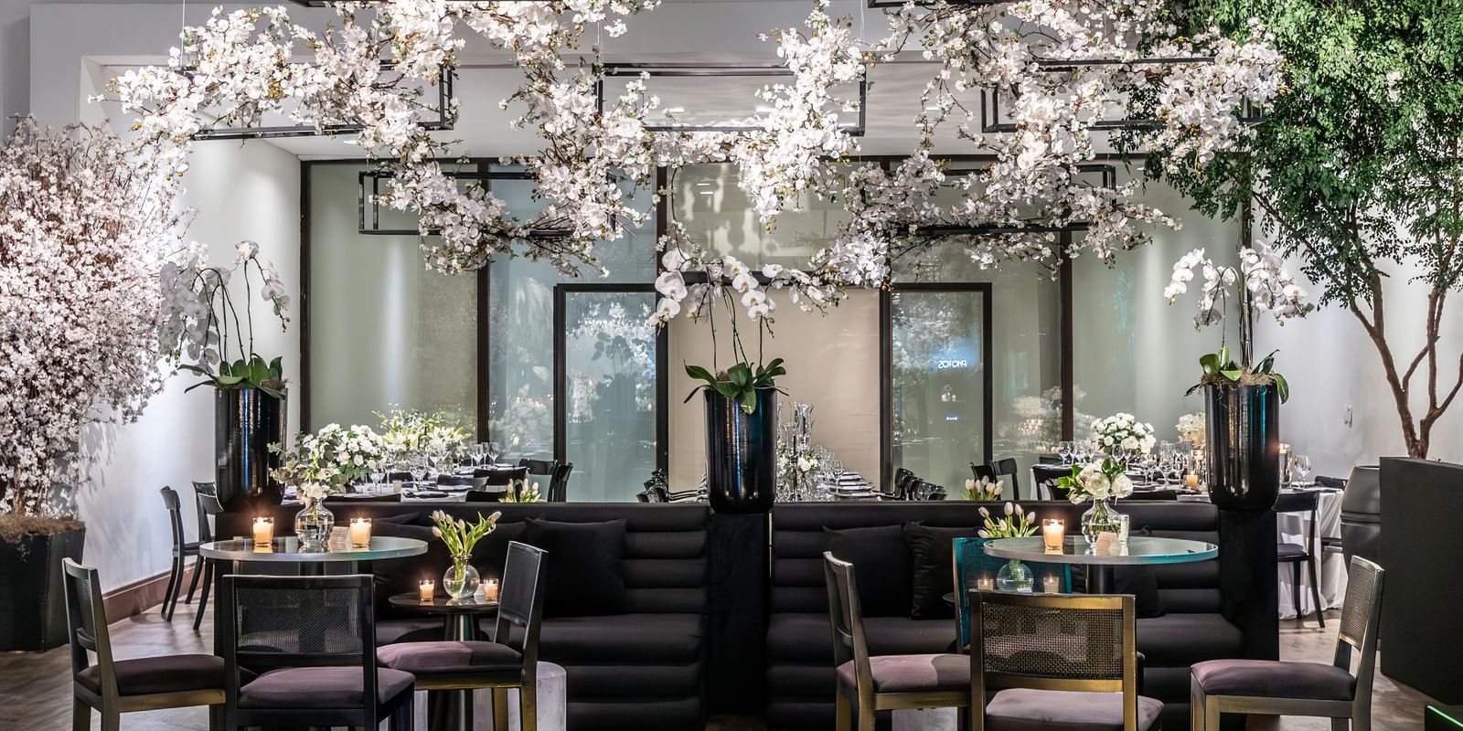 Brightly lit indoor event space with small tables, chairs, and floral decorations.