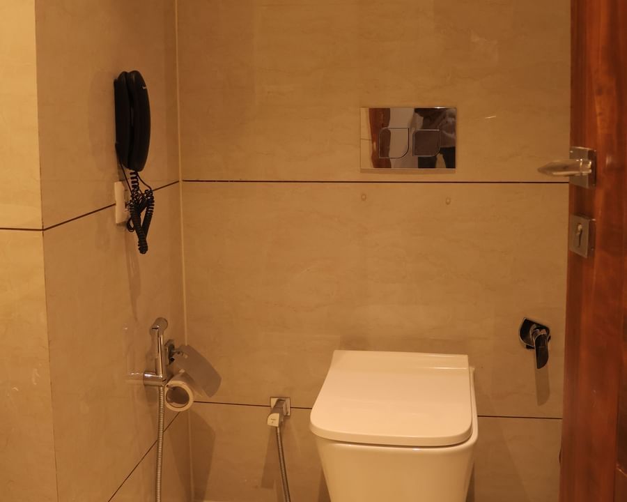 Compact toilet area with wall-mounted WC, framed artwork and handheld shower attachment at Best Western, Vrindavan.