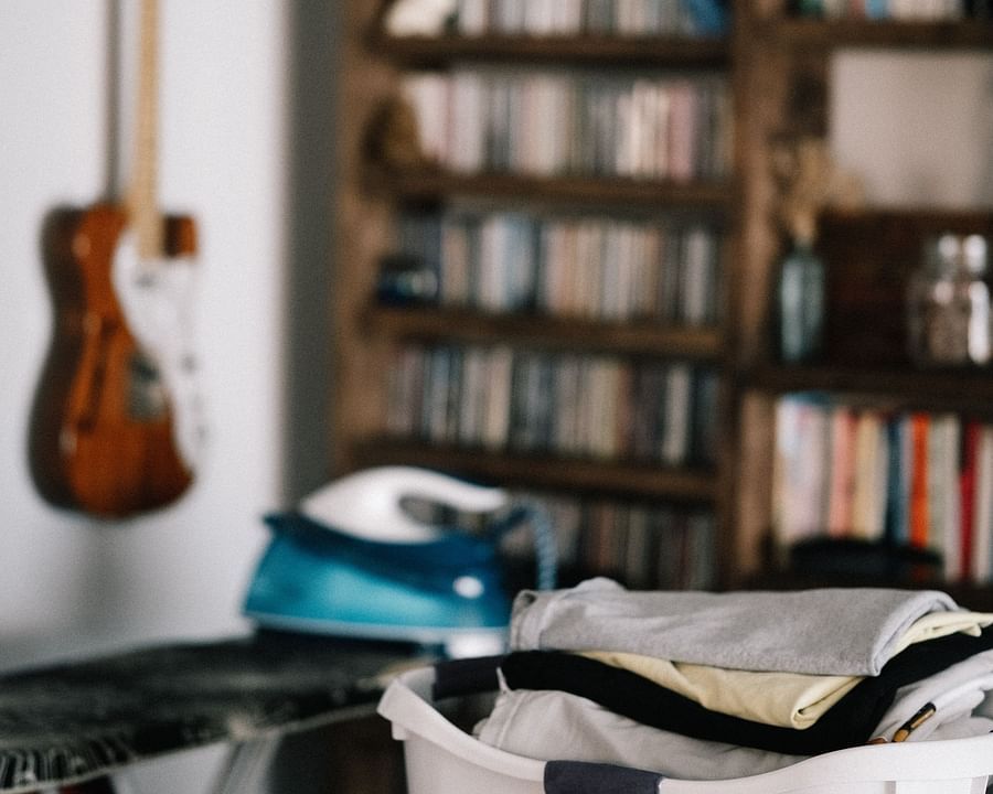 alt-text An image of a basket of fresh laundry placed in a room with a book shelf and guitar hanging on the wall