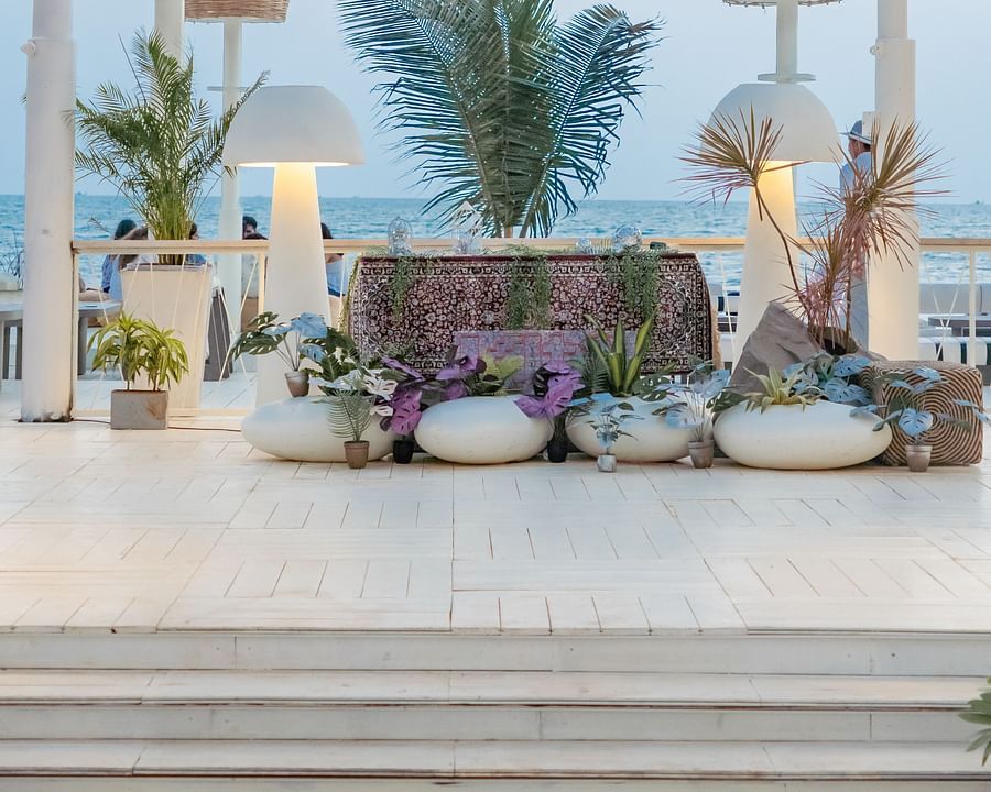 A luxurious outdoor lounge area at Living Room Beach Resort, Morjim, Goa featuring white planters holding lush green plants, illuminated by stylish lamps, all set against a backdrop of the ocean.