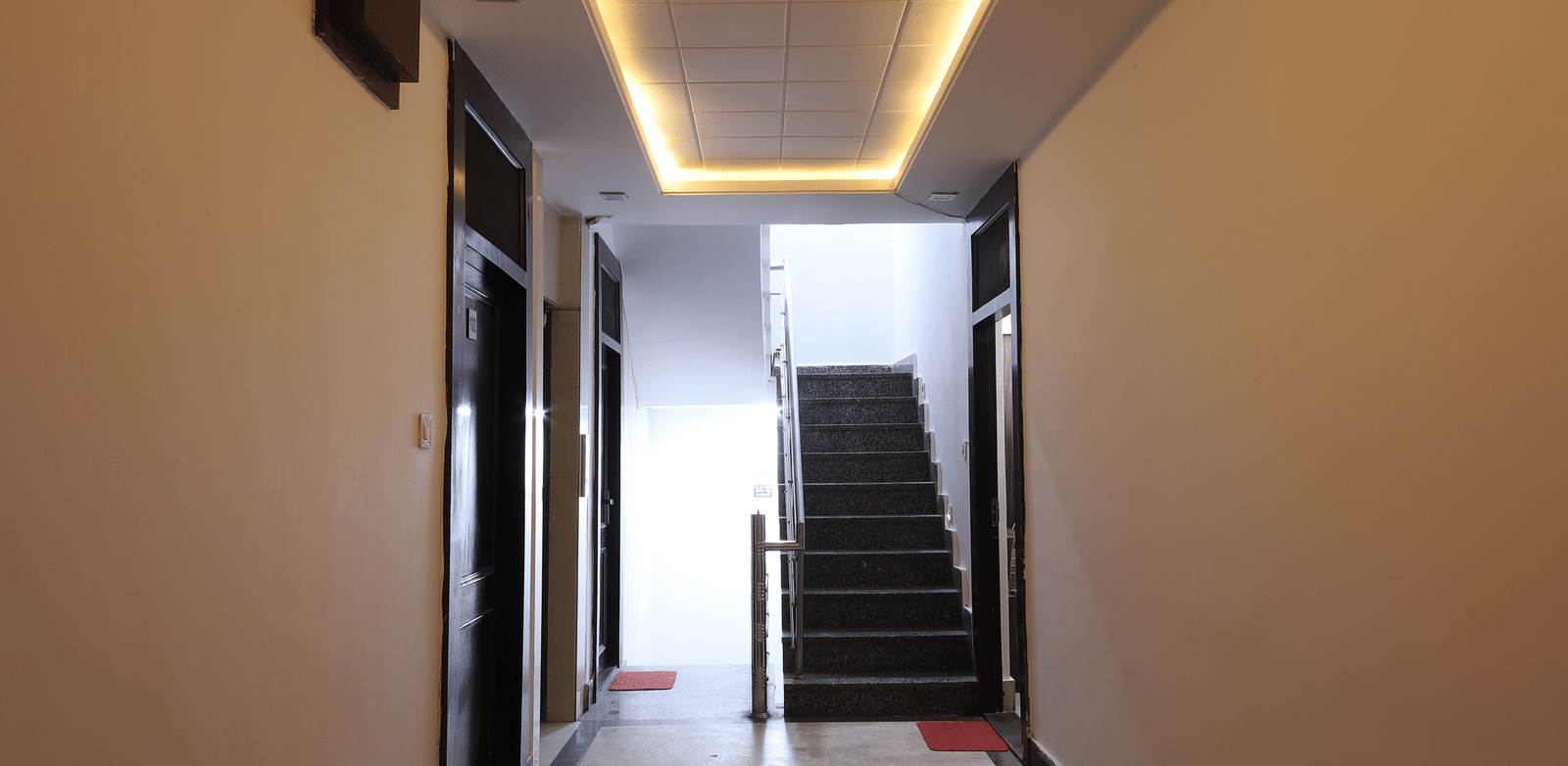 View down a simple hotel corridor with overhead lighting strips and plain walls - Perfectstayz Value Grey Castle, Haridwar