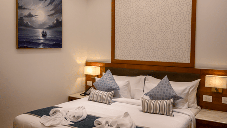 A cosy bedroom layout showing a king size bed decorated with folded towels, a wall painting, and a bedside lamp at Tiara by MPS.