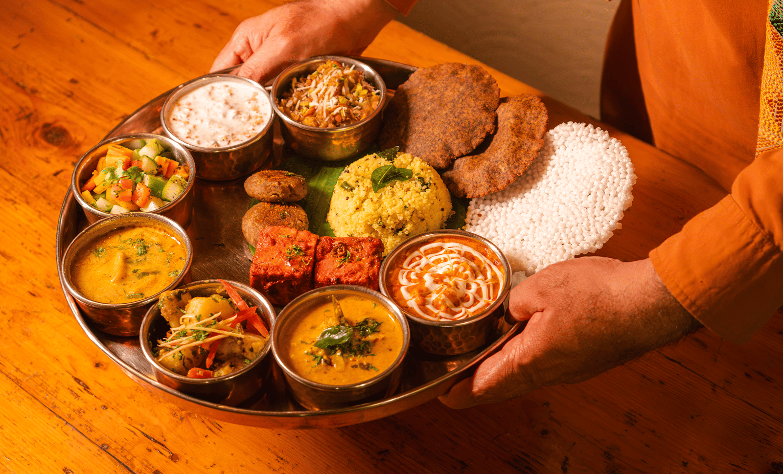 A server presenting the Navratra Feast thali with vrat curries, raita, puris and sabudana papad at Dhaba, The Claridges New Delhi