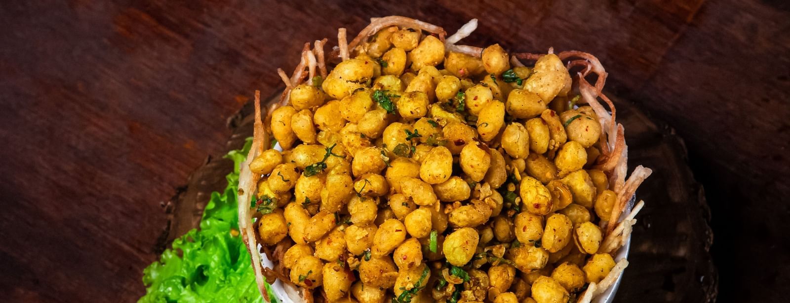  A bowl of appetiser garnished with herbs, served on a wooden platter with lettuce and lime wedges on a rustic wooden table at The Hamuse Hotel, Kodaikanal.