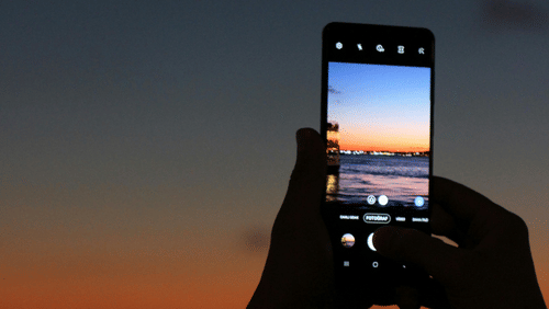 A person clicking the picture of a beach during the late evening hours on their phone.