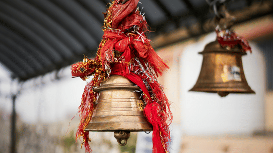 Temple bells with red sacred threads hanging in a place of worship.