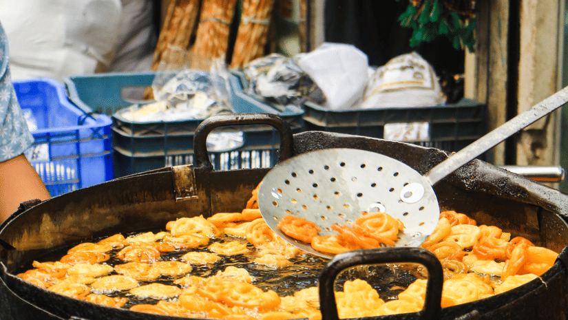 Close up of a huge black vessel where piping-hot jalebis are getting fried at a small confectionery shop in India.