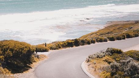 an aerial view of a winding road near the beach with waves in view