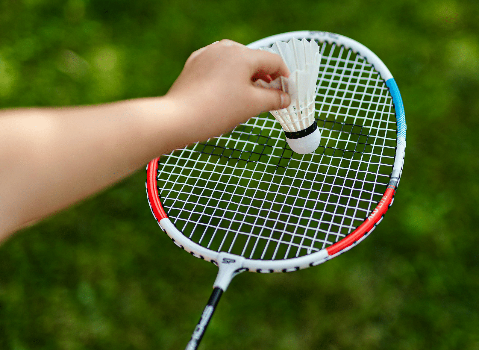 A person preparing to serve, holding a shuttlecock against a racket