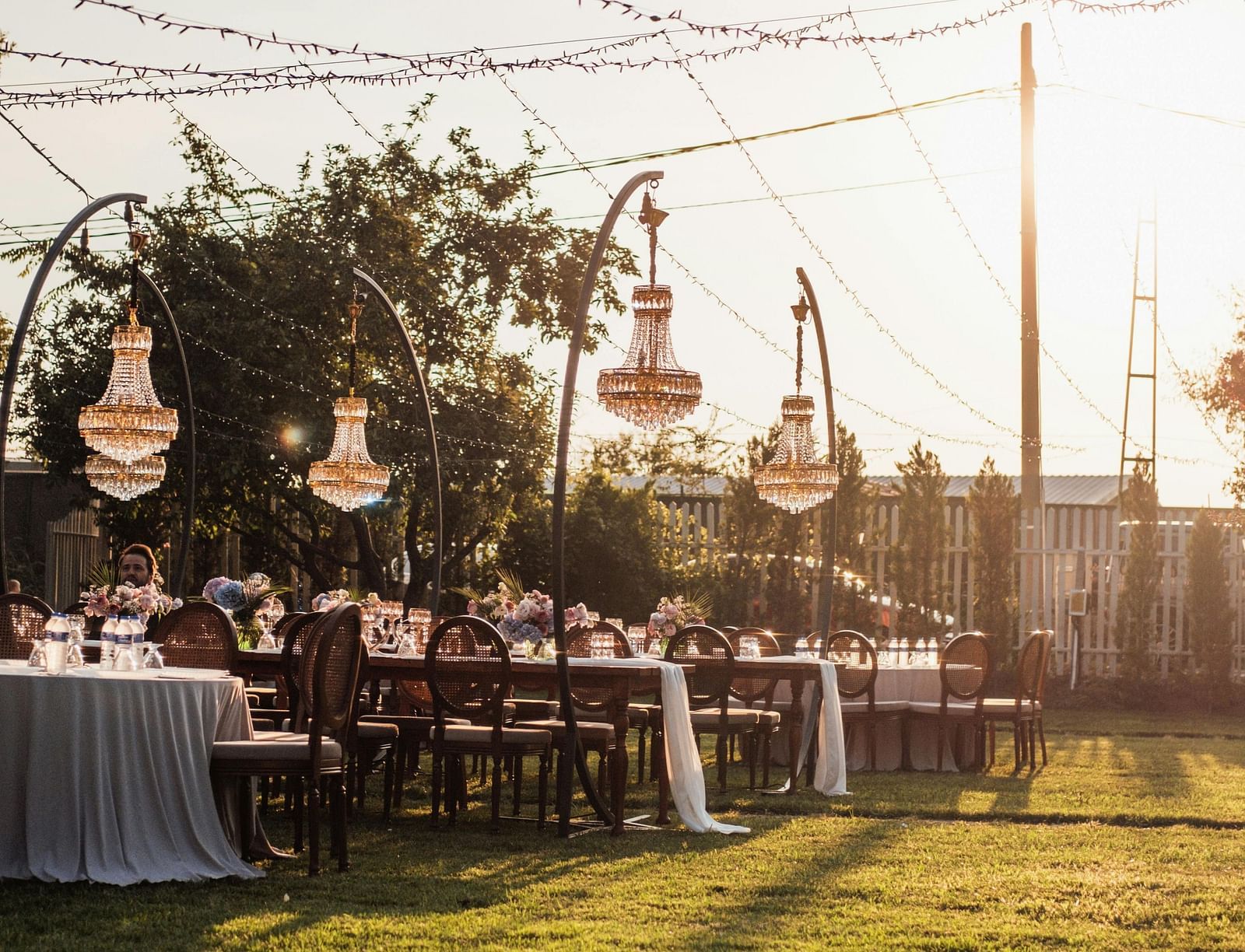A beautiful lawn area with tall poles holding the decorative strings with a bright sun setting in the background.