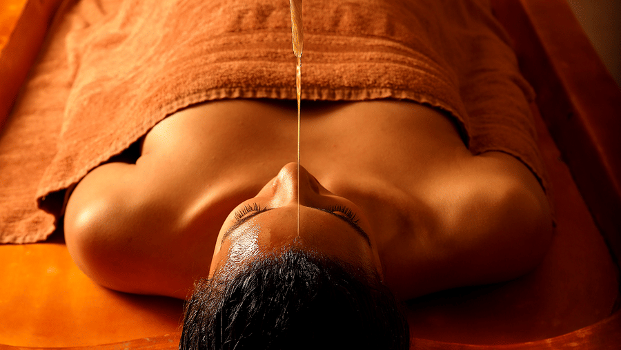 A person lying on a table receiving an Ayurvedic oil therapy on the forehead at Heritage Village Resorts & Spa, Manesar, one of the best luxury spa resorts near Delhi